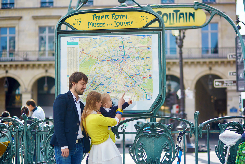A woman and her partner stand at a map and navigate the public transportation system while also holding onto a toddler.