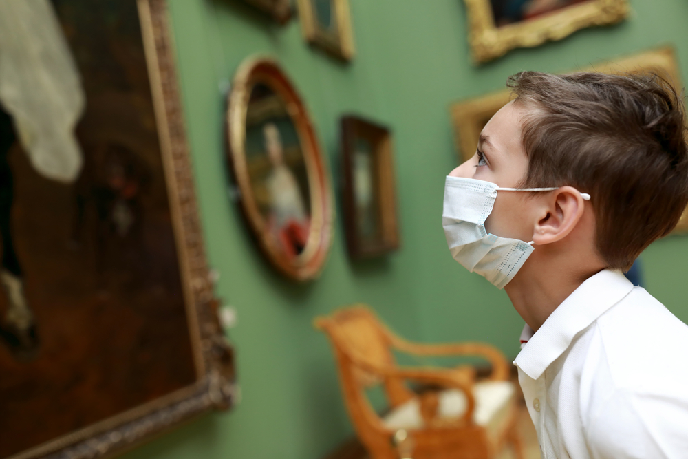 A young boy in a mask and white shirt peers up at a famous art piece: museums are a great way to entertain children in Paris! 