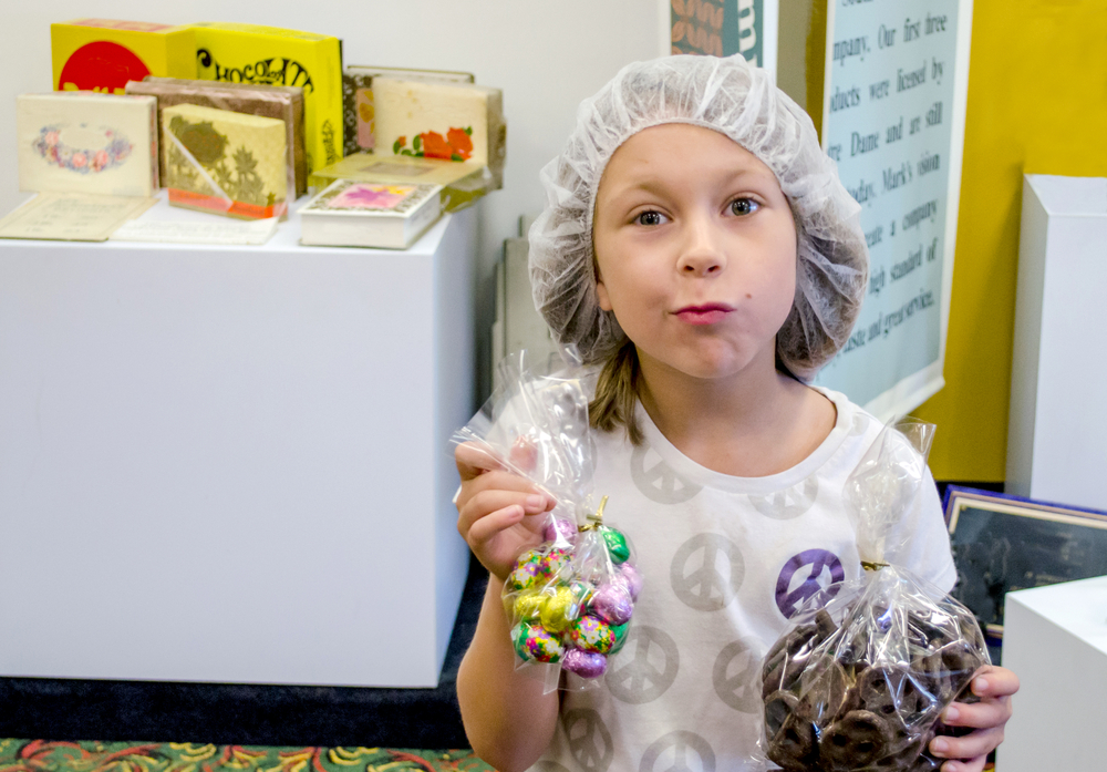 A young girl holds bags of chocolates and wears a hairnet after watching chocolate demonstrations at museums!