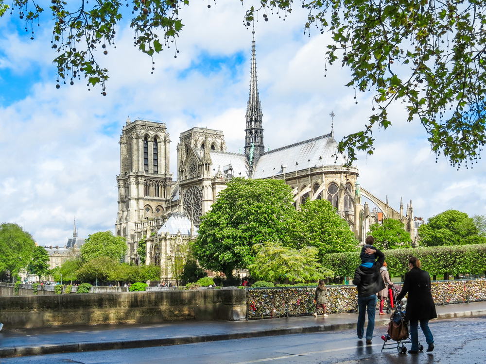 A family pushing a shoulder stop and pause to look at Notre Dame: of all the things to do with kids in Paris, strolling and sightseeing is a great option!