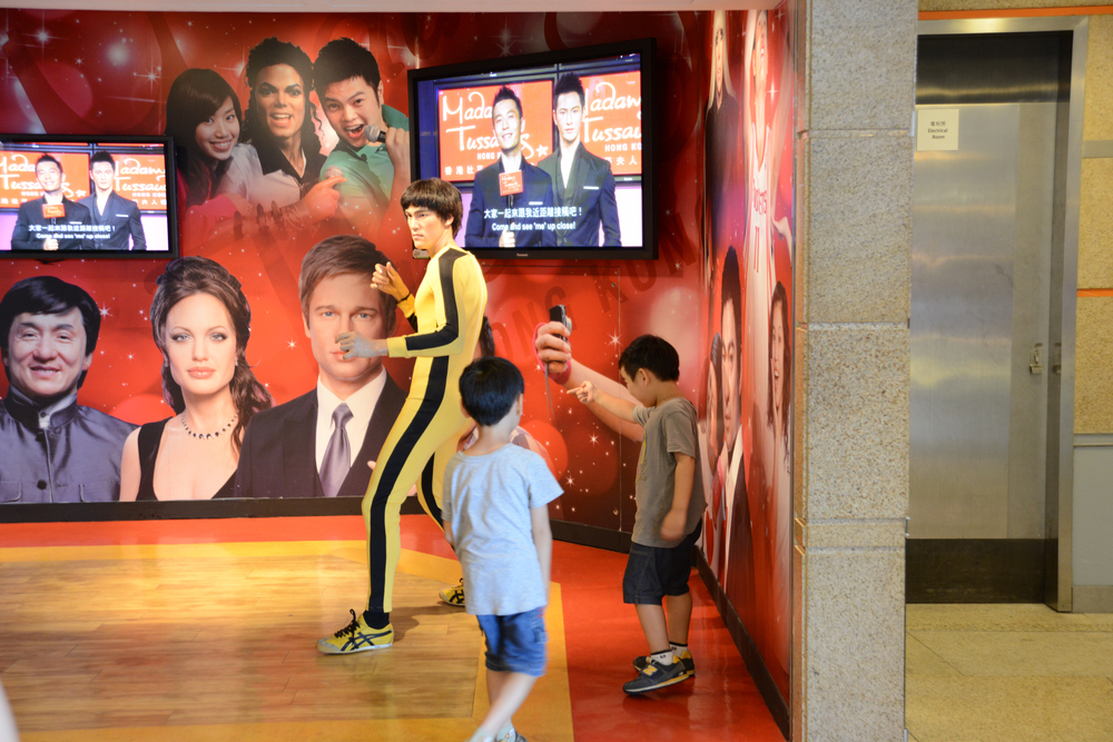Two young boys approach a wax figurine who is in a yellow sports suit and is posed so the kids can take photos with him.