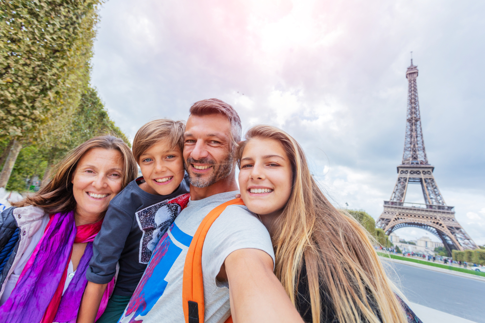 A family of four smiles for a selfie with the Eiffel Tower in the background: they are ready to go climb to the second floor.
