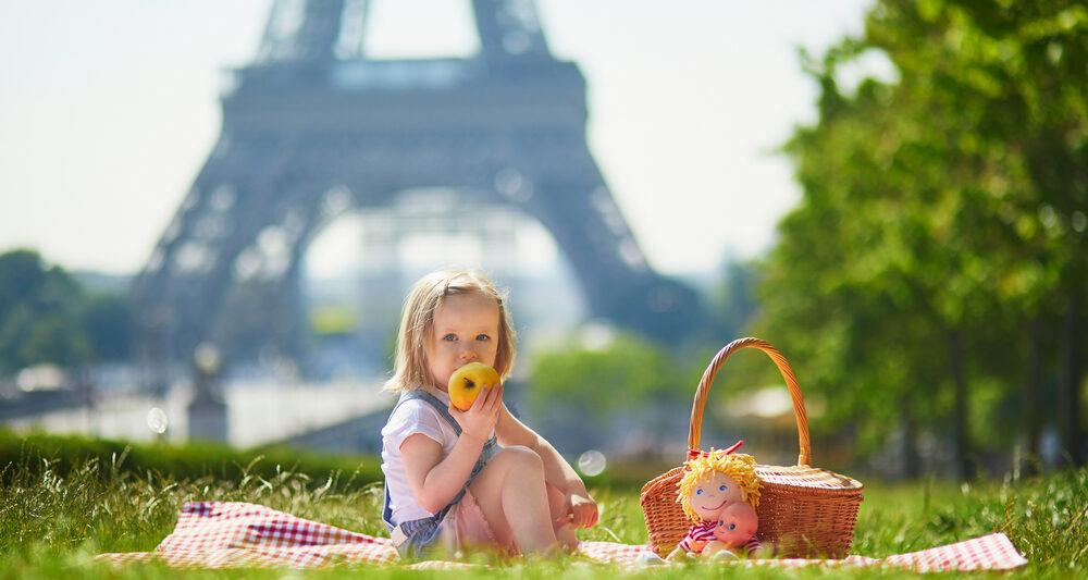 child in paris sitting in front of tower eating an apple