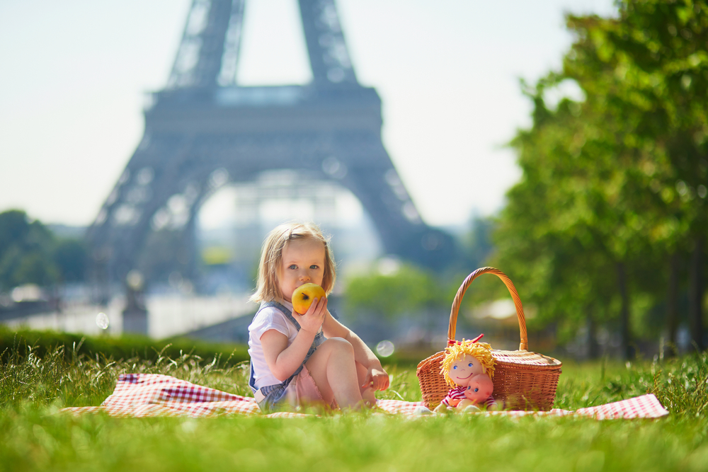 A young girl munches on an apple in front of the Eiffel Tower: of all things to do with kids in Paris, keeping it simple works well!