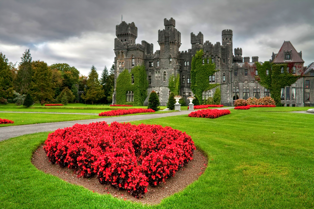 Cloudy day at Ashford Castle with patches of red flowers in the lawn.