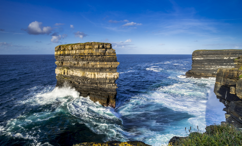 Ocean water swelling around a colorful sea stack off the coast of Ireland.