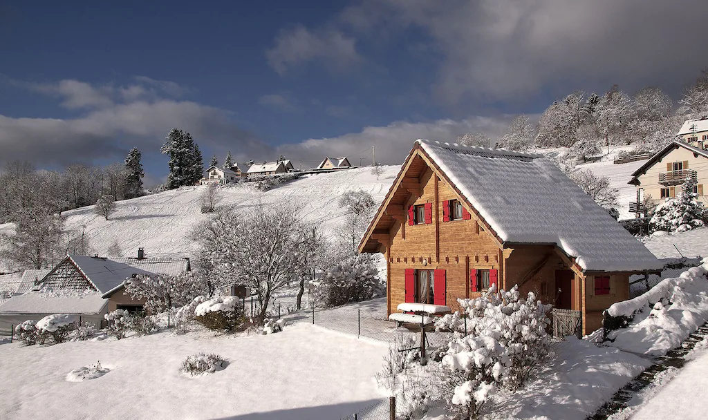 View of a wooden chalet with cute red shutters, covered in snow. 