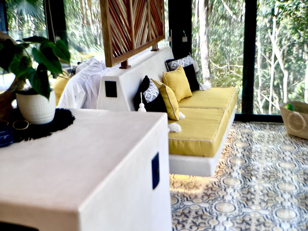 View of the picturesque yellow cushions, tiled floor, and beautiful jungle beyond in the Tulum Reflection Loft. 