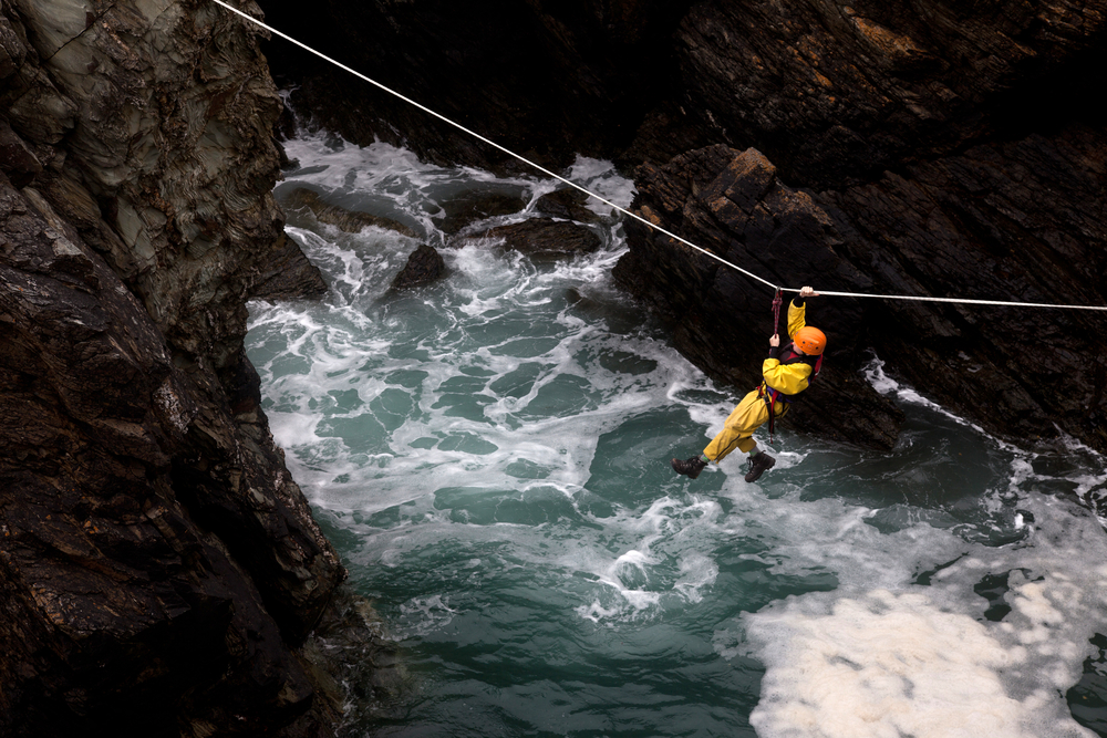 Person on a zip line between cliffs over the sea.