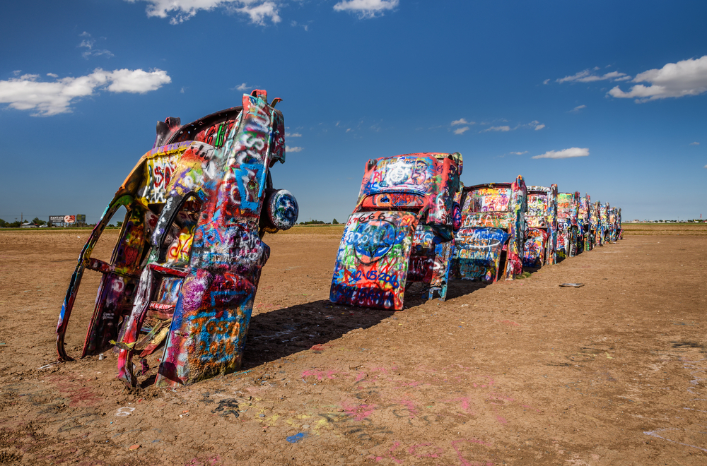 Line of colorful, graffitied Cadillacs sticking up in the air in a line in a desert.