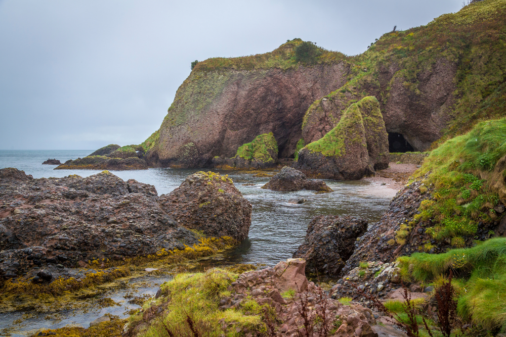 Rocky shore leading to the moss covered Cushendun Caves on a cloudy day.