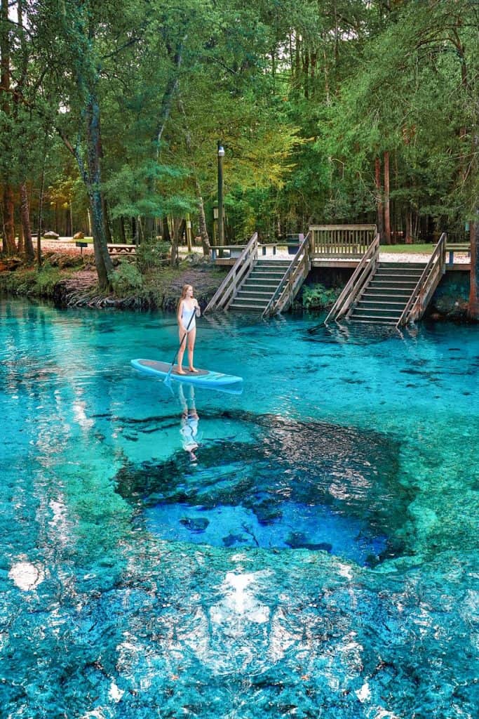 A woman on a stand up paddle board at Ginnie Springs with vividly blue water.