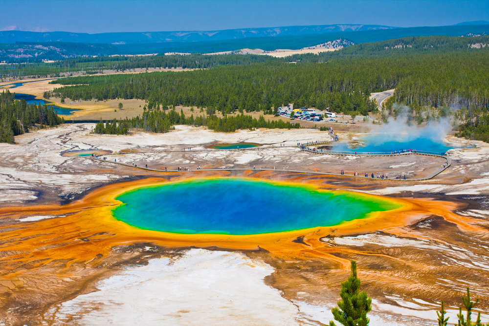 a photo of old faithful in Yellowstone with pretty colors and mountains in the back 