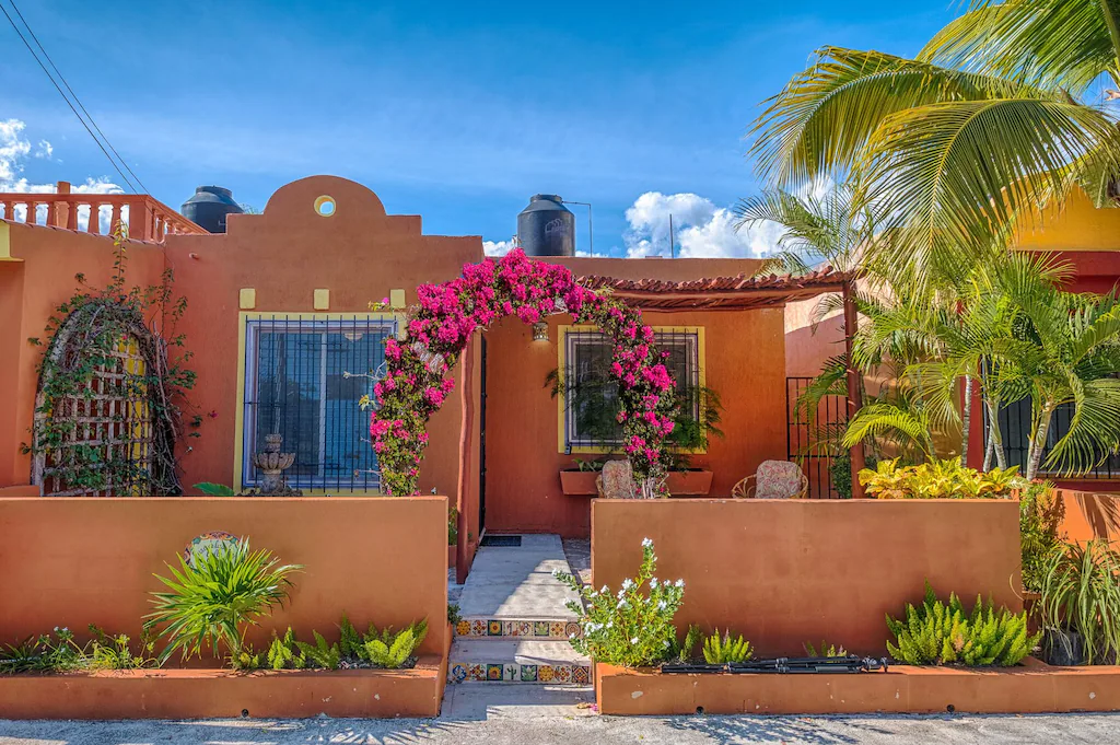 View of the traditional adobe exterior and lush front garden full of hot pink flowers of the Casa de Las Joyas 