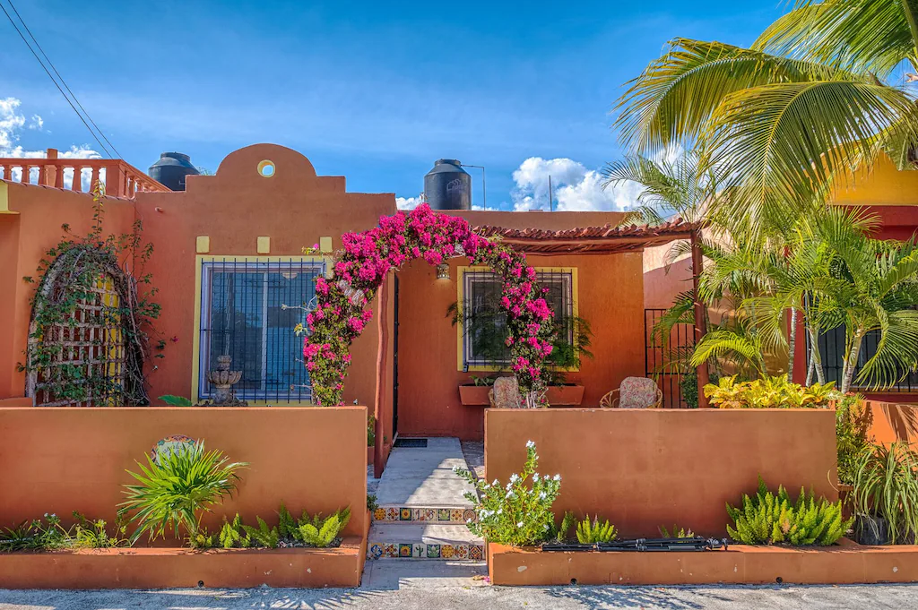View of the traditional adobe exterior and lush front garden full of hot pink flowers of the Casa de Las Joyas