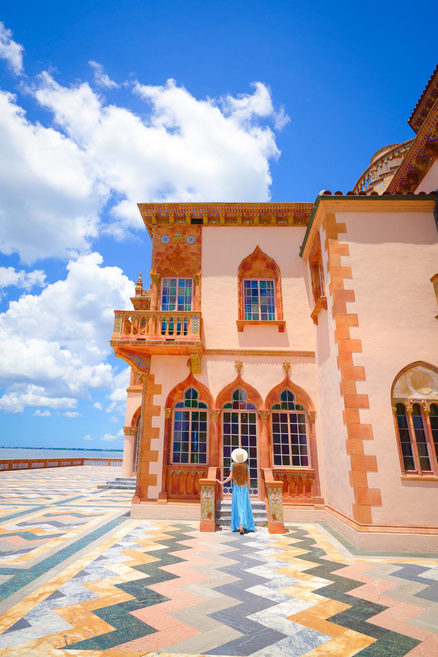 A girl in a blue dress facing away from camera in front of the pink mansion at the Ringling Museum in Saraosta.