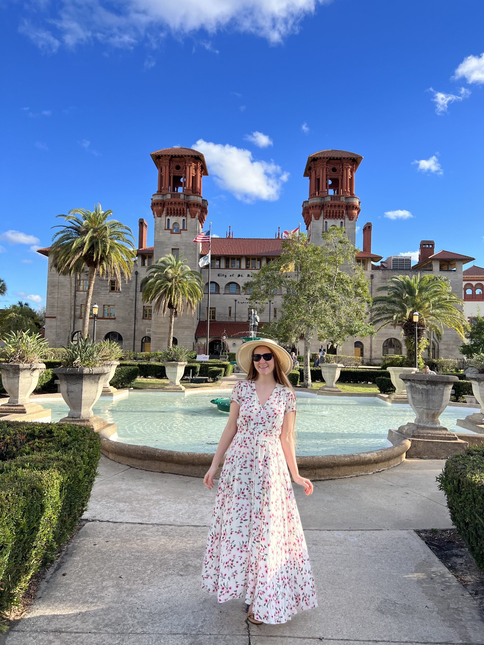 a girl in a summer dress with hat standing in front of a fountain and historic building in Saint Augustine one of the BEST things to do in Florida