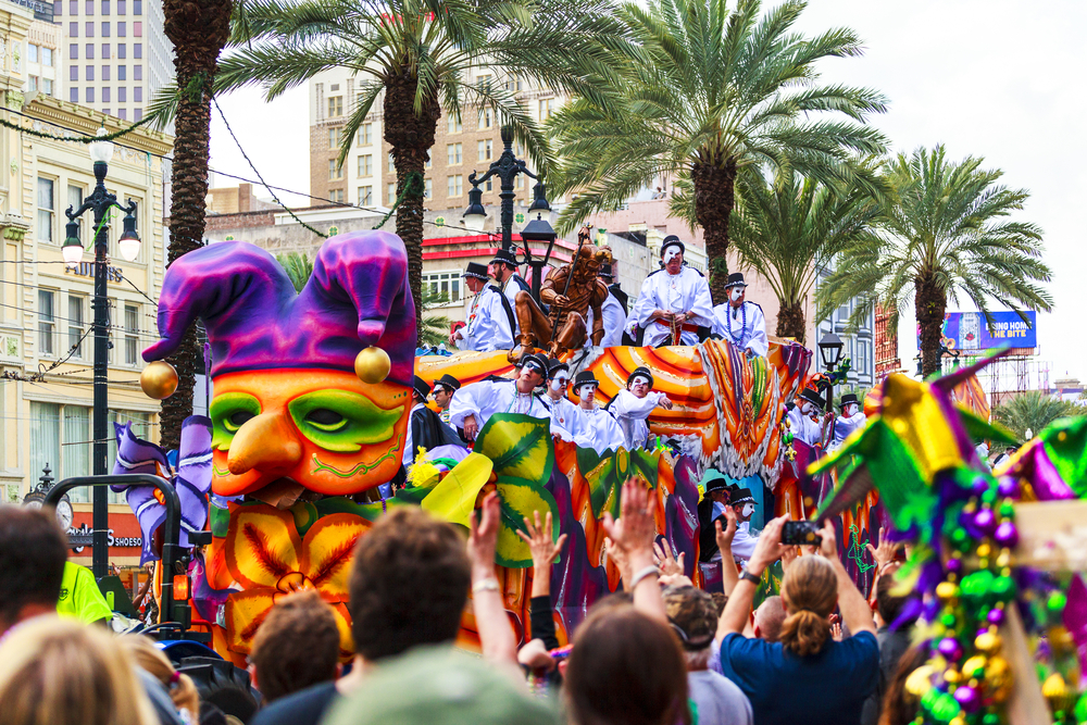 a madre gras parade full of people celebrating in the street and a big colorful float. this is one of the best winter vacations in the USA