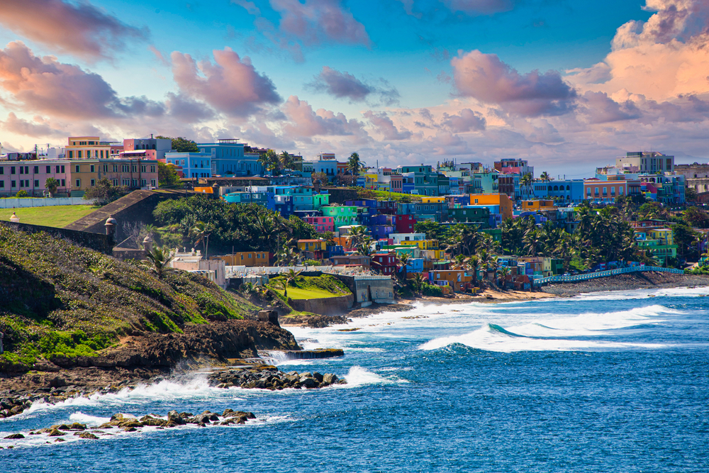 the colorful buildings of old San Juan in the winter time. the sea is blue with big waves crashing on shore 