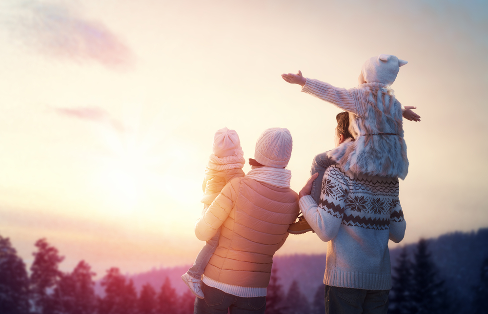 a family on their winter vacation in the  US looking at the sun set with big coats and hats in the snow. 