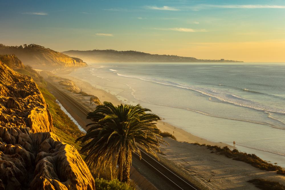 a beautiful beach in san Diego CA in the winter time at sunset. there are palm trees, small waves, and beautiful mountains 