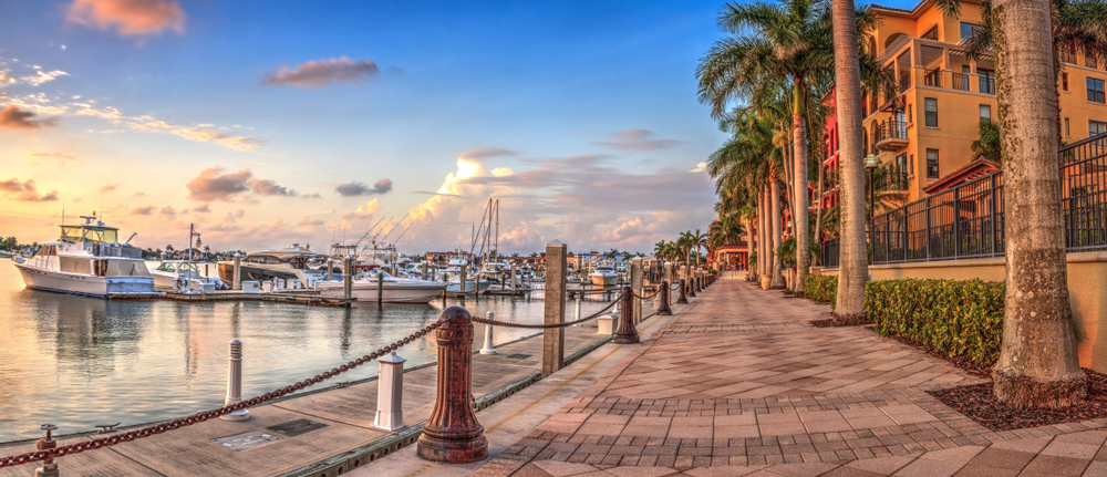 the harbor of Marco Island with boats and a paved brick pathway with palm trees at sunset time