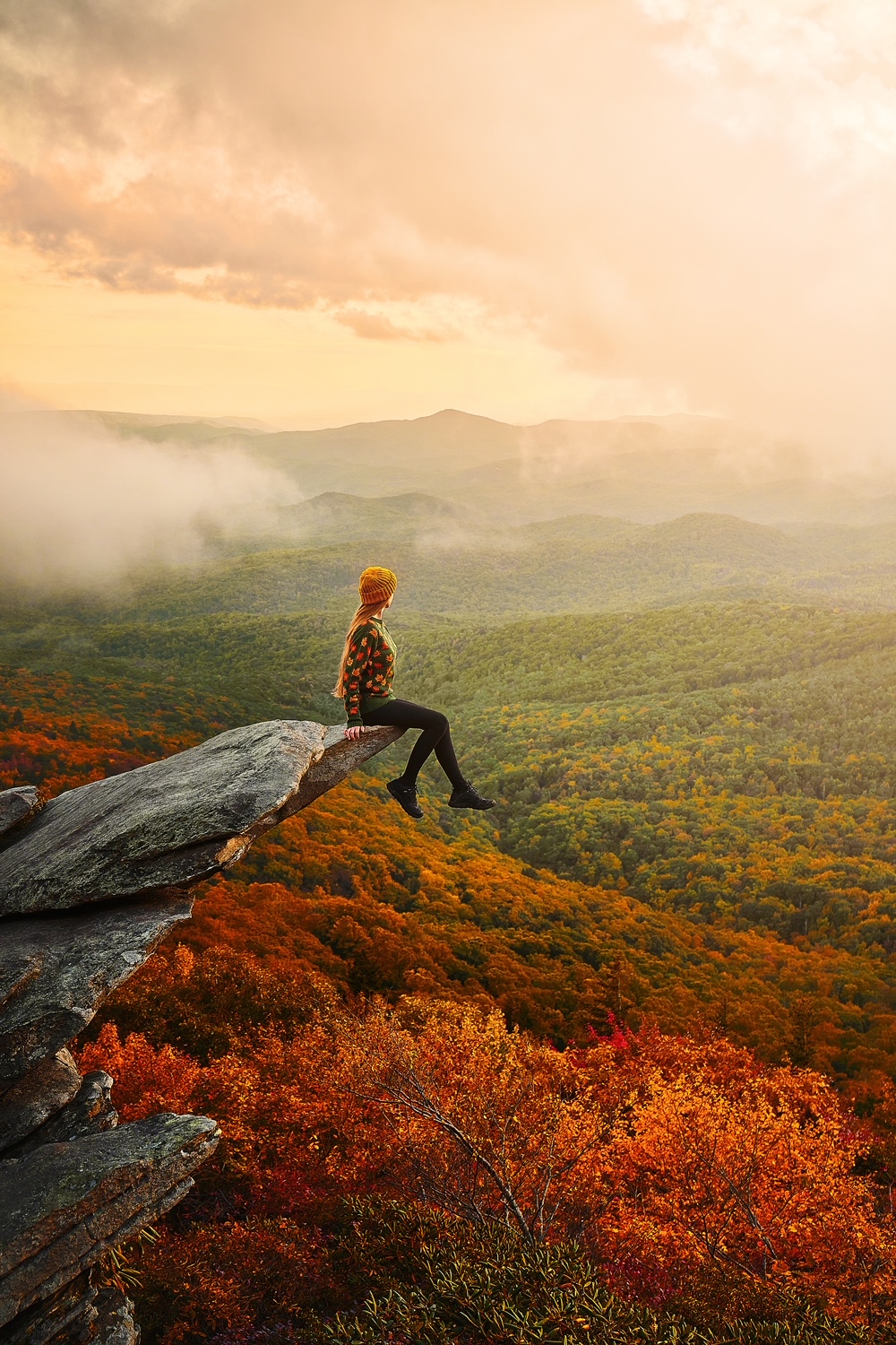 Woman sitting on a ledge overlooking hills of fall foliage the USA.