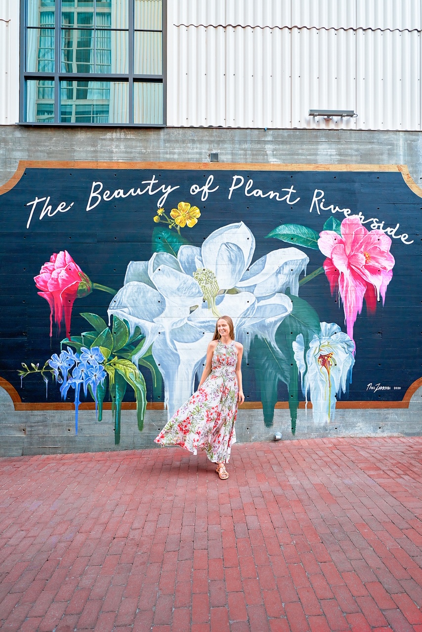 a girl in a flowery dress in front of a hand painted mural and red brick street