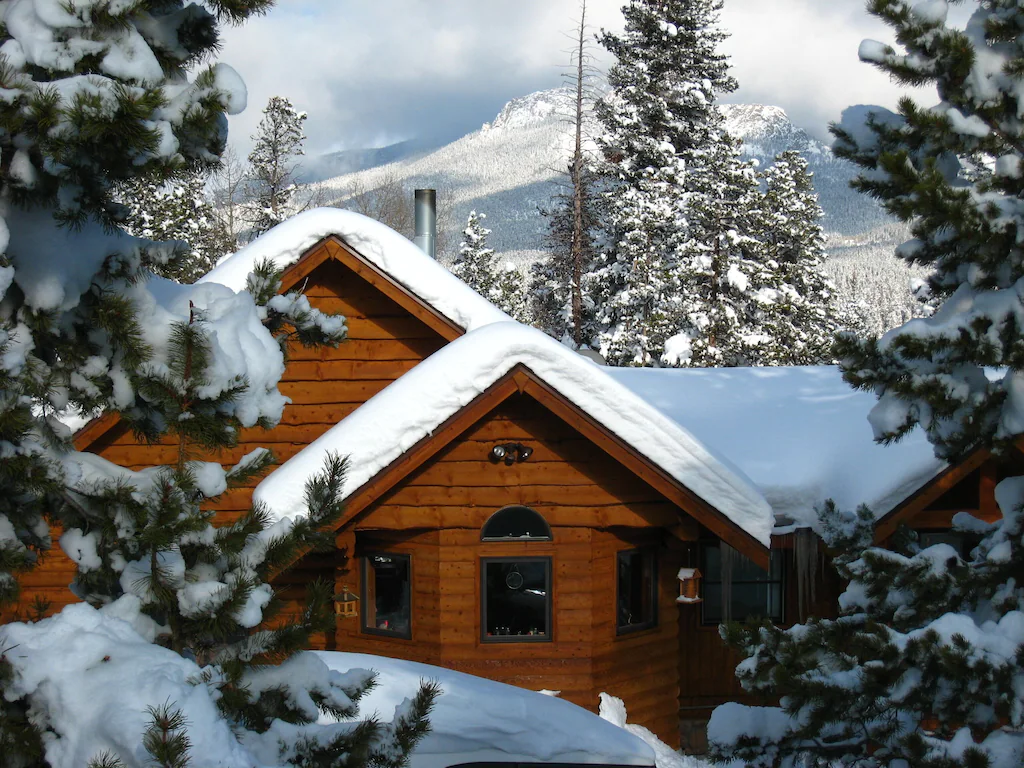 view of a log cabin covered in snow with a large mountain in the background