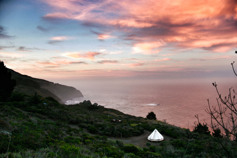 A white tent sits overlooking the coast in Big Sur, Cali during a pink sunset.