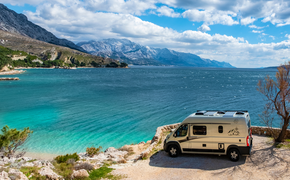 An RV overlooks the cusp of the clear water and sits across from huge mountains in Hawaii: Hawaii has many of the top locations for the best beach camping in the USA. 