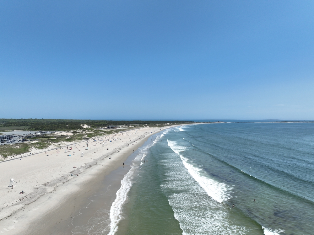 A long stretch of coast in Massachusetts shows people gathering on the beach: you can actually camp on the sand here, making it one of the best beach camping in the USA.