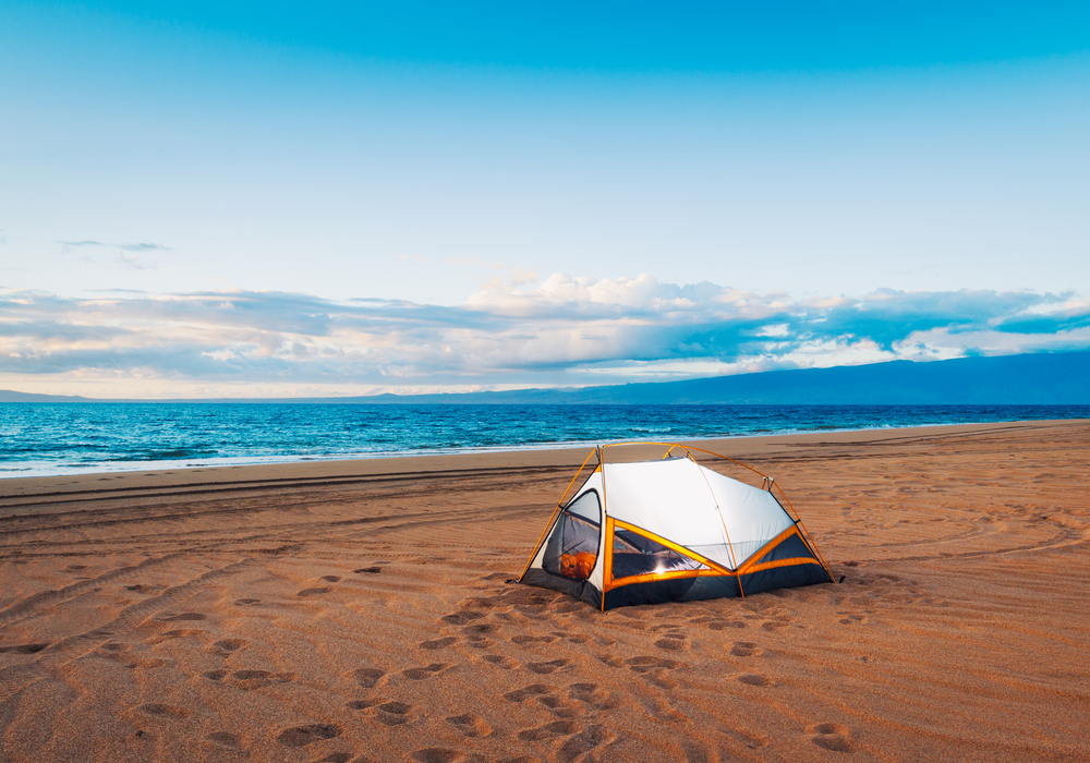 A single tent sits on the sand and overlooks the clear, blue water in Mississippi, which surprisingly has a few options for the best beach camping in the USA. 
