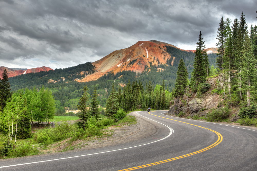 A road cutting through trees with a mountain in the distance during a Colorado road trip itinerary.