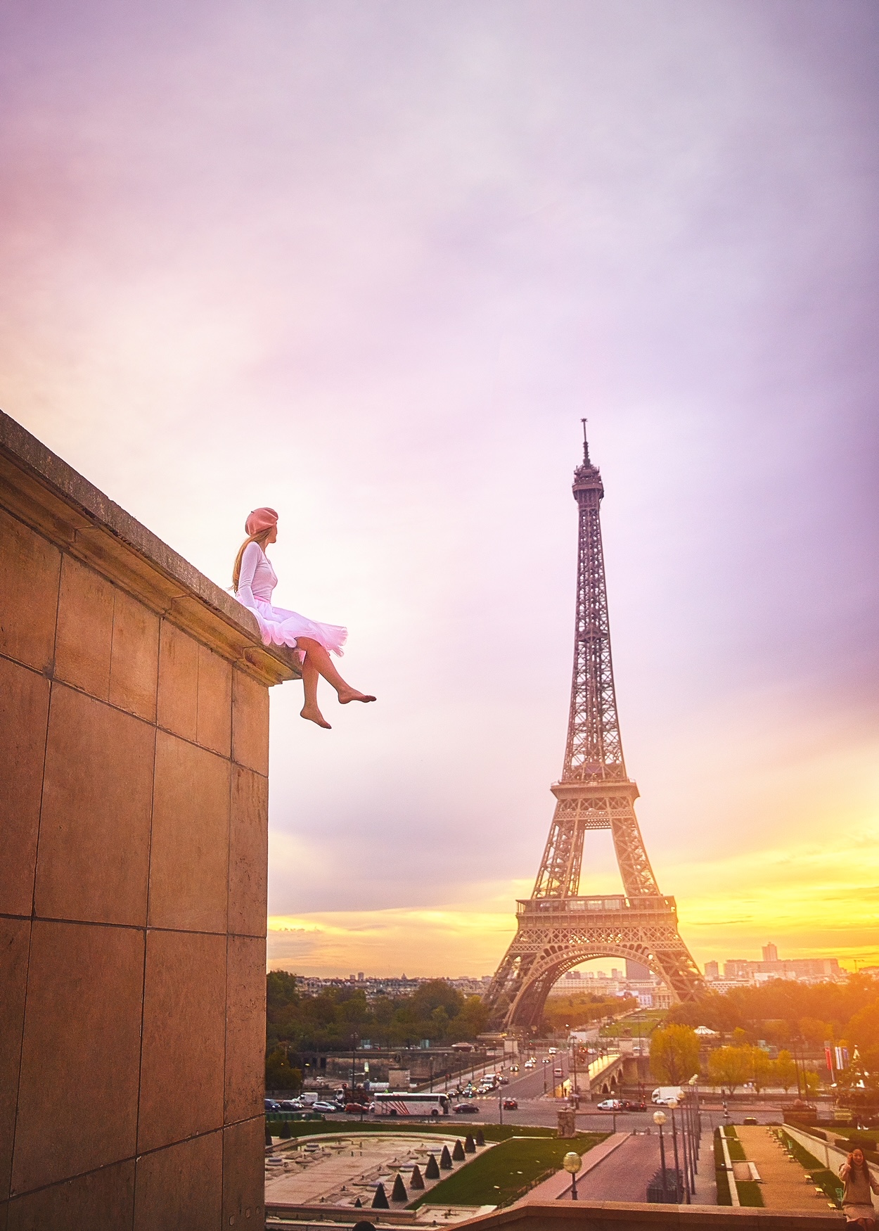 Sunrise over the Eiffel Tower with a woman in a shirt sitting on the edge of Place du Trocadero.