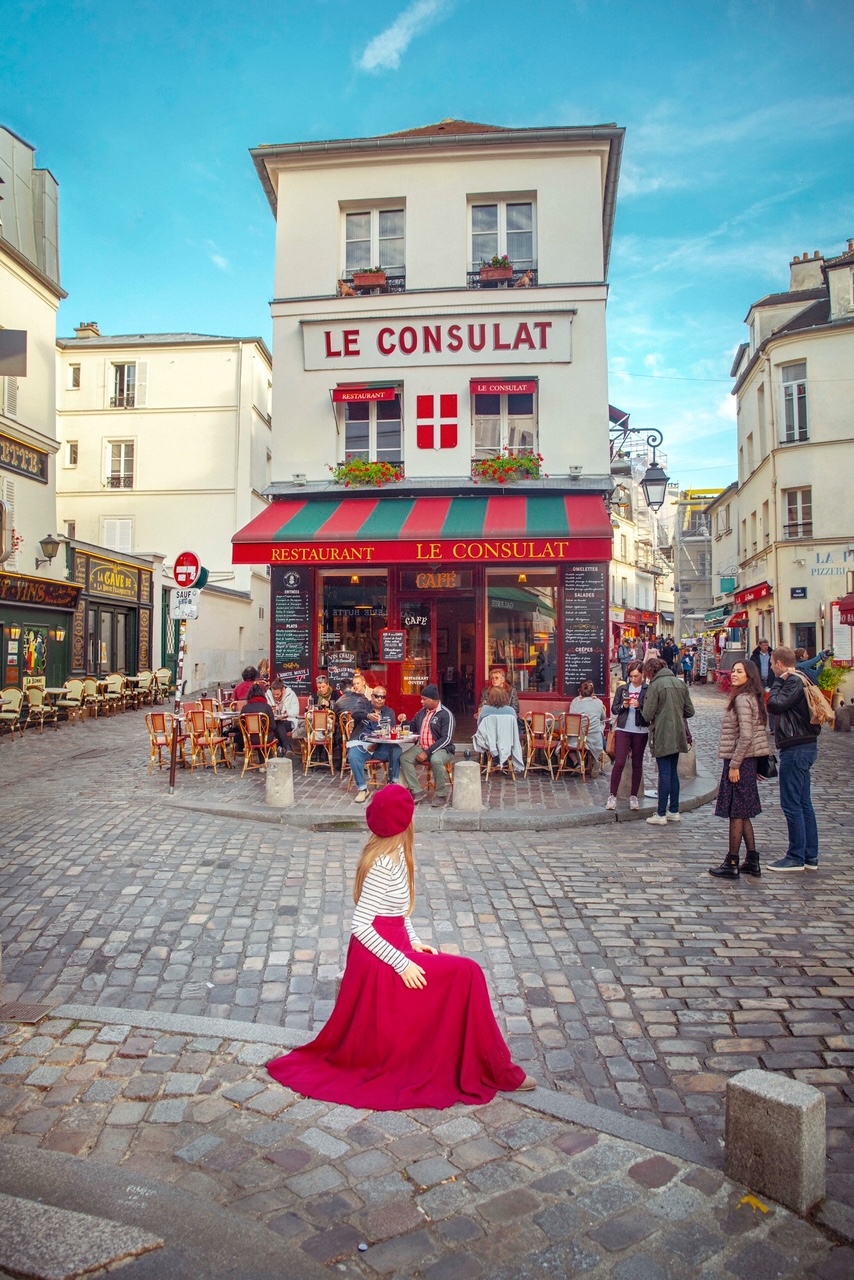 Woman in red skirt stands in front of Le Consult in Paris.