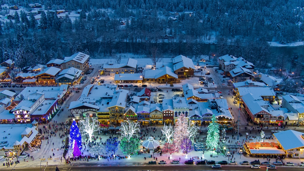 the town of Leavenworth from above with the German christmas market lite up in the middle. the town is covered in snow and looks very festive 