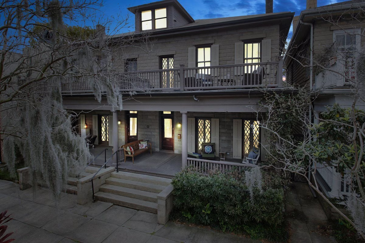 Exterior of the cozy boutique carriage house, lit from within and surrounded by trees covered in Spanish moss. 