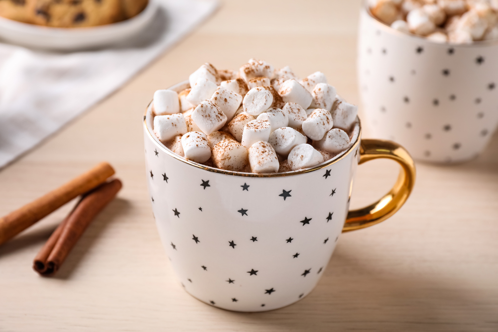 a warm cup of hot chocolate covered with a mound of mini marshmallow, sticks of cinnamon!