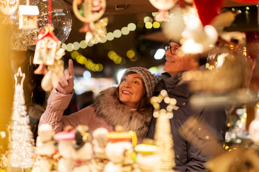 Two individuals enjoying each others company and loving some hand made goods at an artisans booth at a market with lovely bright holiday lights!