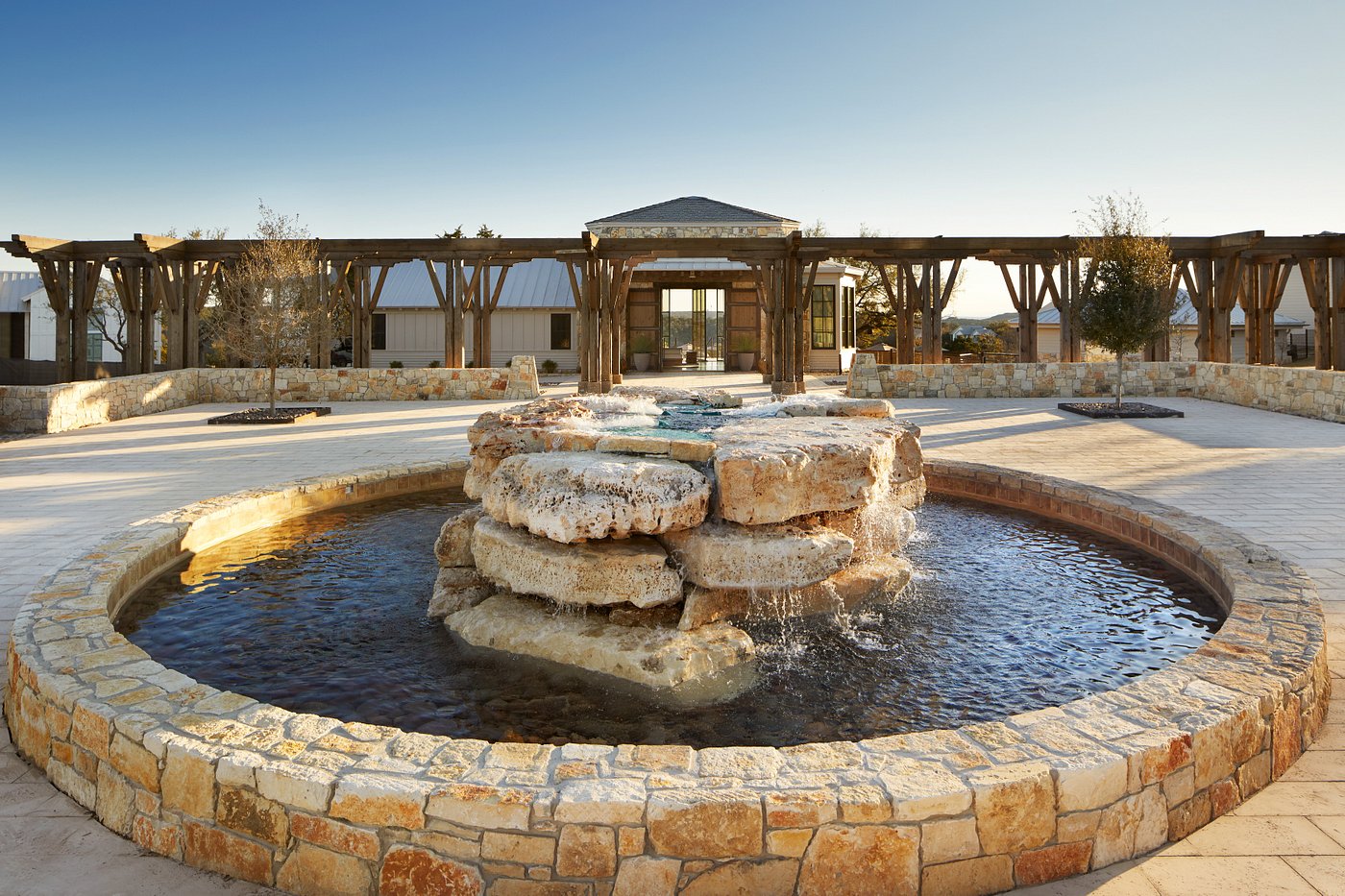 a fountain with water rolling off of large granite rock slabs and beyond it is large, beautiful building in the background, the perfect glam spot for a time of relaxation at one of the all inclusive resorts in Texas!