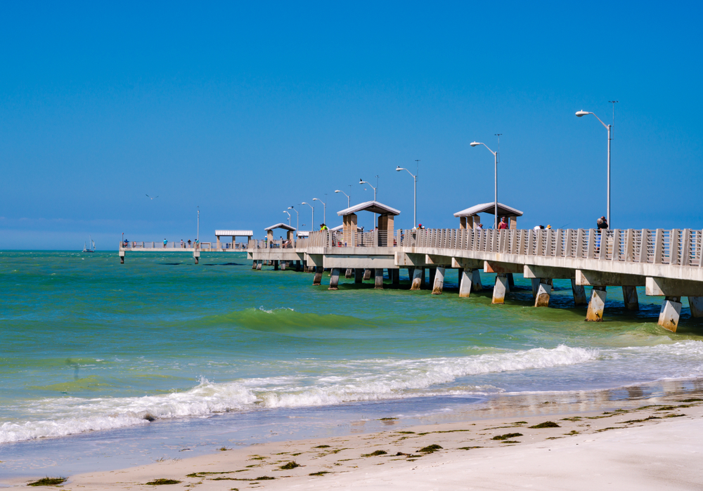 The teal water of Fort De Soto's beach crashes against a pier filled with people. 