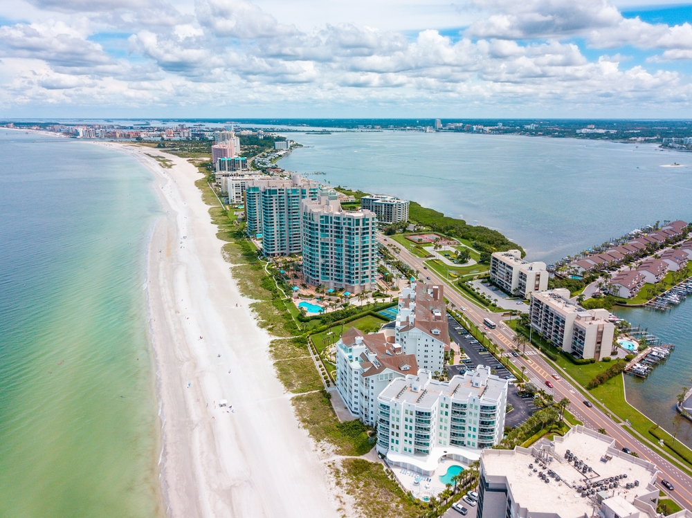 An arial shot of Sand Key shows a strip of white sand, blue water, and tall buildings and hotels. 