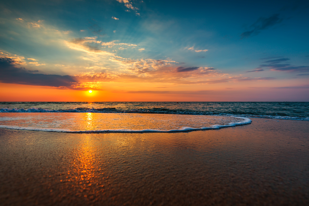 An orange sunset kisses the water as waves lap at the shore at one of the best beaches in Tampa FL. 