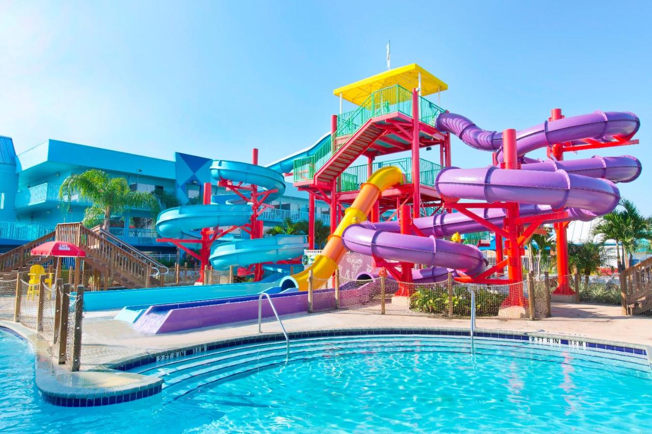 a slide tower with three colorful slides, a pool in the foreground on a clear sky day 