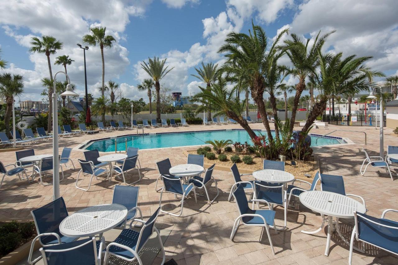 table and chairs surrounding a pool, palm trees and other vegetation are around the pool as well, clouds in the sky at Orlando waterpark resort 