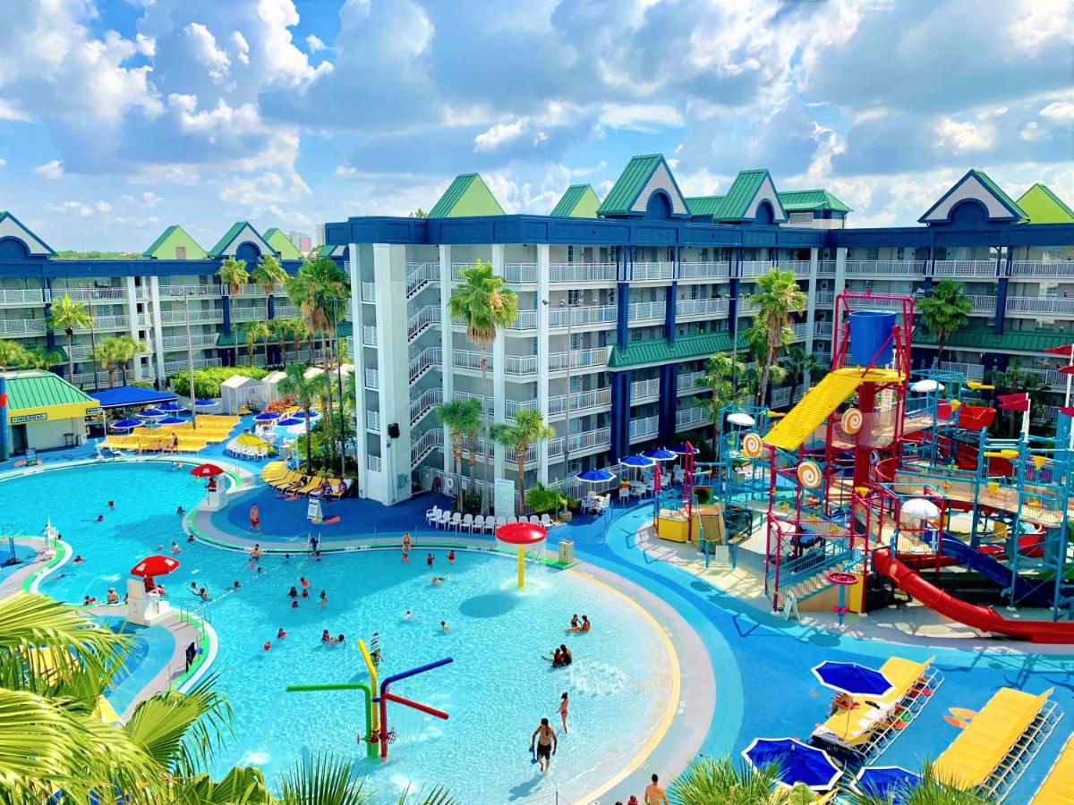 a large pool on the left and a tall water park tower on the right. in the background there is two hotel buildings 