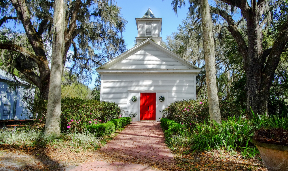 tall, willowy trees with nicely trimmed hedges and bushes in front of a pure white forest chapel with a bright red door at the front!