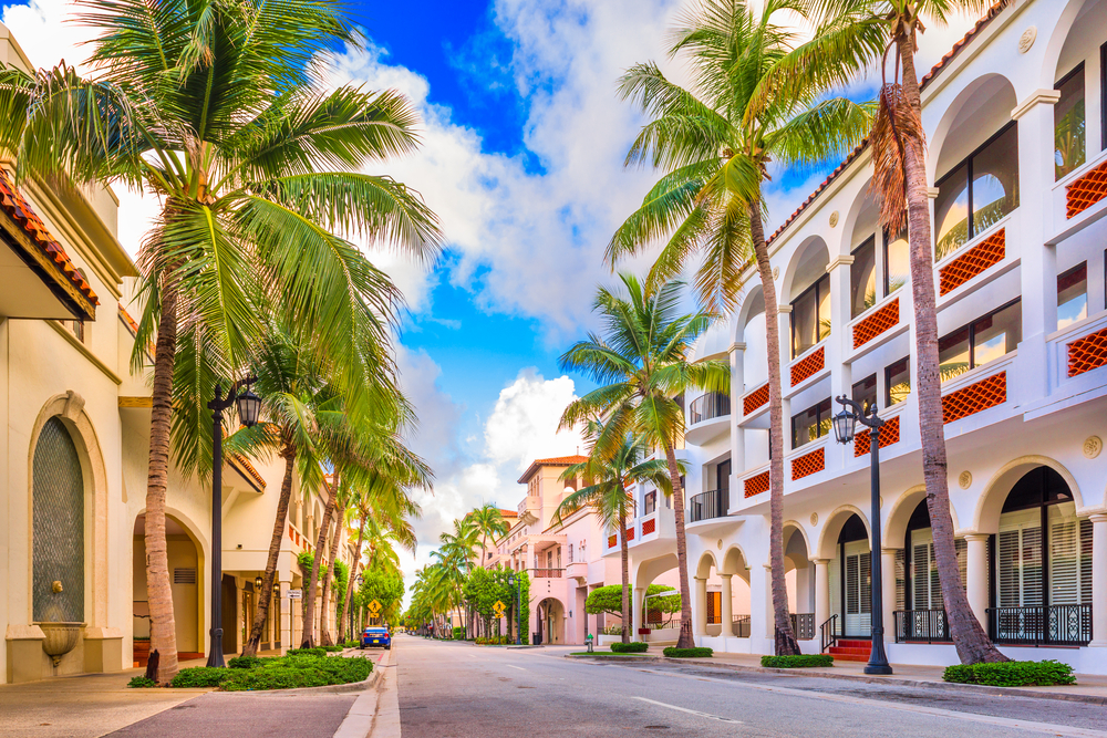 beige and white buildings with large palm trees on either side of a road leading through the center of the city!