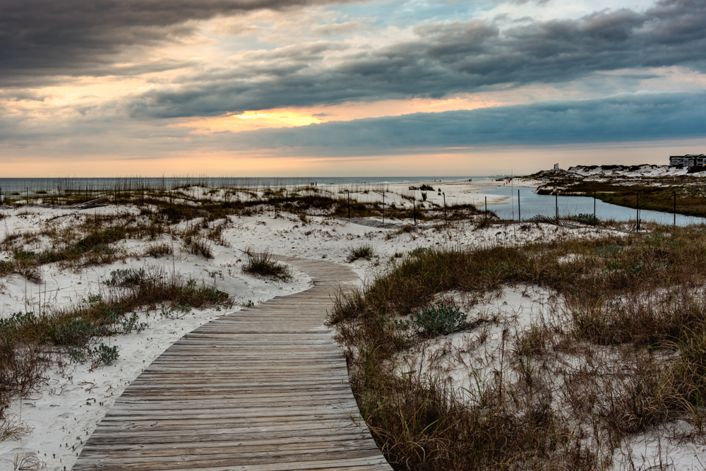 a dusky storm sky with white sand and grassy sections with a winding planked pathway down to the water!